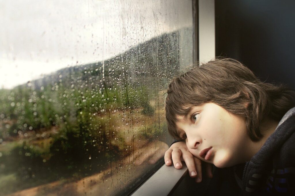 物憂げに雨が降る外を見つめる少年